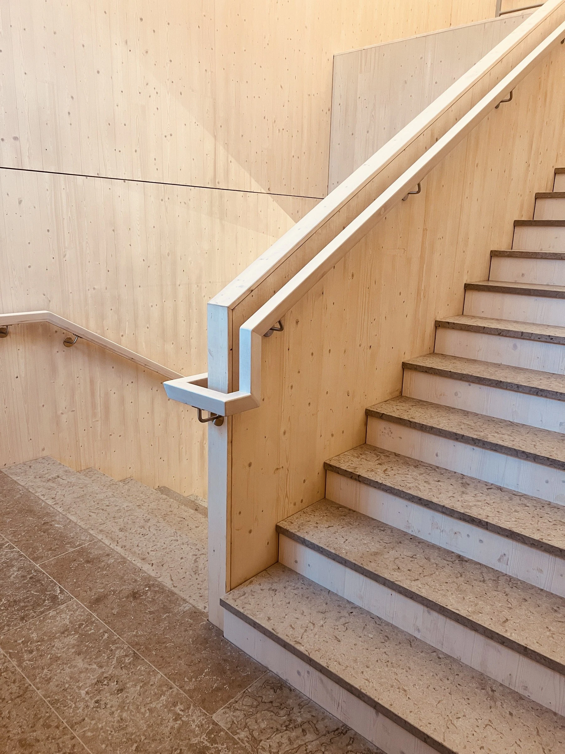 Pale timber staircase with stone treads and integrated angular handrails